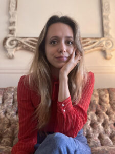 Photo de Holly Vestad. Elle a de longs cheveux blonds et le teint clair et porte sa main gauche à son visage. Elle porte un chandail rouge rayé.