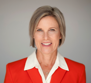 Portrait de Lucy Payette. Lucy a les cheveux blonds courts, les yeux bleus et le teint clair. Elle porte une veste rouge avec un chandail blanc en dessous.