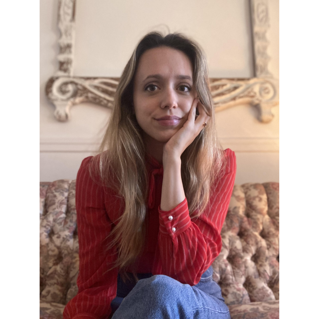 Photo de Holly Vestad. Elle a de longs cheveux blonds et le teint clair et porte sa main gauche à son visage. Elle porte un chandail rouge rayé.