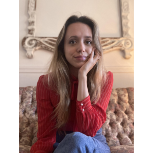 Photo de Holly Vestad. Elle a de longs cheveux blonds et le teint clair et porte sa main gauche à son visage. Elle porte un chandail rouge rayé.